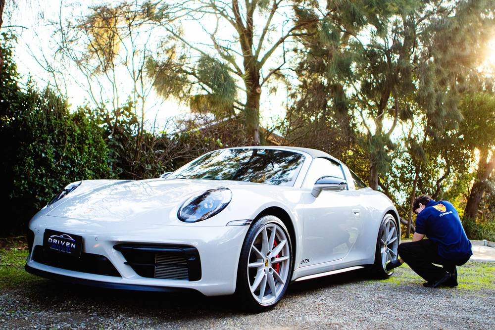 Sebastian detailing a white Porsche 911 GTS in a driveway at sunset